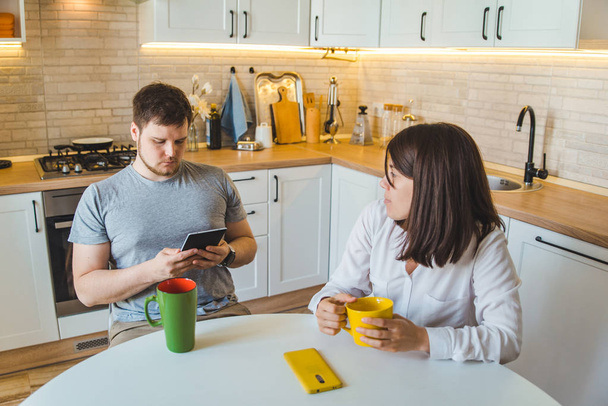ζευγάρι κάθεται στην κουζίνα το πρωί πίνοντας τσάι διαβάζοντας ειδήσεις - Φωτογραφία, εικόνα