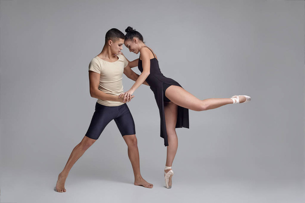 Twee atletische moderne balletdansers poseren tegen een grijze studio achtergrond. - Foto, afbeelding