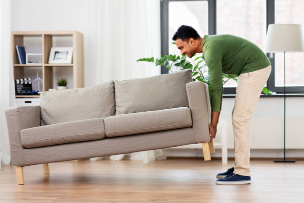 happy indian man moving sofa at home - Foto, immagini