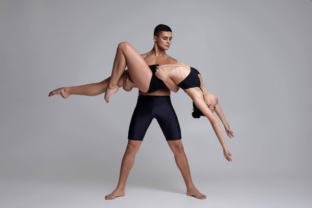 O casal de jovens bailarinos modernos em ternos pretos estão posando sobre um fundo de estúdio cinza
. - Foto, Imagem