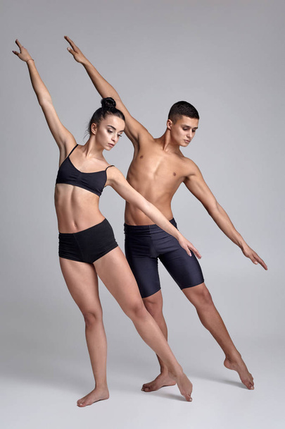 A pár egy fiatal modern balett-táncosok fekete öltönyök pózol egy szürke stúdió háttér. - Fotó, kép