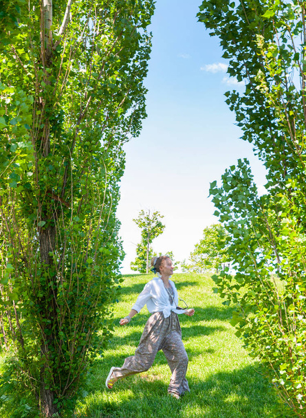 晴れた日に自由を楽しむ美しいボーホスタイルの女の子。緑の草の上にジャンプ陽気な女性 - 写真・画像