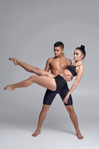 das Paar einer jungen modernen Balletttänzerin in schwarzen Anzügen posiert vor grauem Studiohintergrund. - Foto, Bild