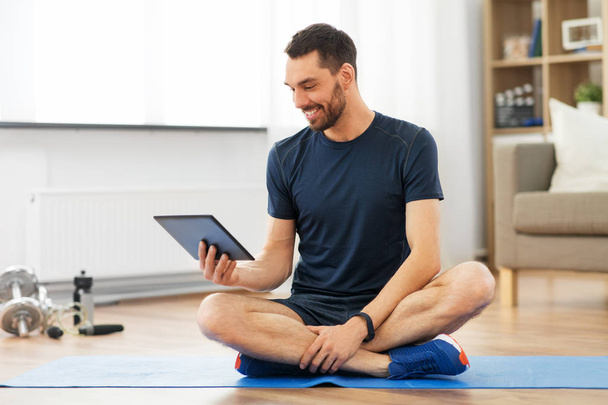 man with tablet computer on exercise mat at home - Foto, Imagen