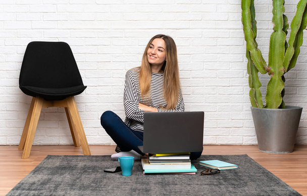 Genç kadın onun laptop gülüyor ile yerde oturuyor - Fotoğraf, Görsel