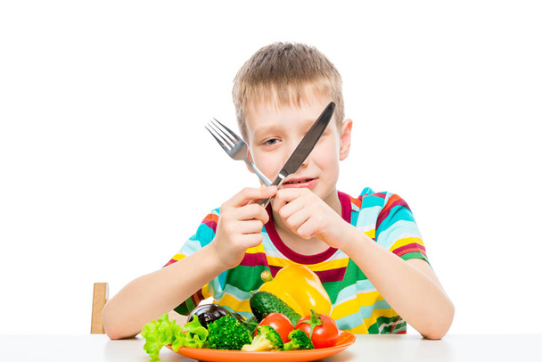 αγόρι με ένα μαχαίρι και πιρούνι τρώγοντας φρέσκα ωμά λαχανικά, πορτρέτο  - Φωτογραφία, εικόνα