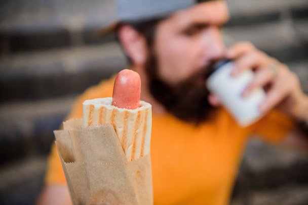 What a sausage. Hipster drinking coffee with hotdog snack on stairs outdoor. Caucasian guy enjoying snack on street. Bearded man snacking with unhealthy sandwich snack. Snack and food - Foto, Imagen