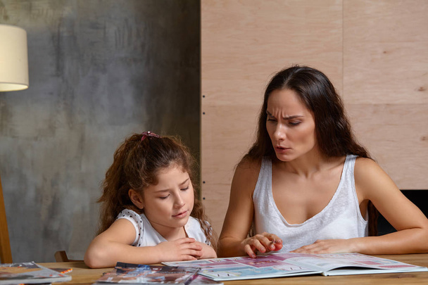 Портрет матері, яка допомагає своїй маленькій милій доньці зробити домашнє завдання в приміщенні. Щаслива сім'я
. - Фото, зображення