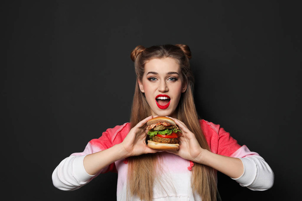 Pretty woman with tasty burger on black background - Foto, immagini