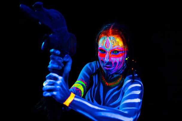 Portrét mladé nahé divoké ženy v modré zářící ultrafialové barvy s prvotní předhistorickou tomahawovou zbraní. Nejvyšší avatar bojovnice s účesu - Fotografie, Obrázek