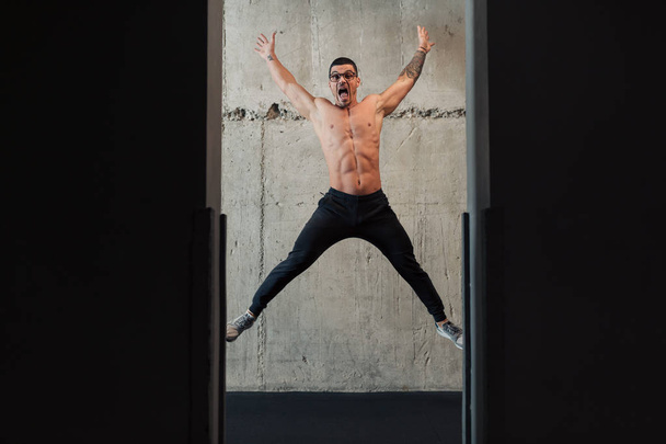Молодий сильний чоловік в окулярах біля бетонної стіни стрибає
 - Фото, зображення