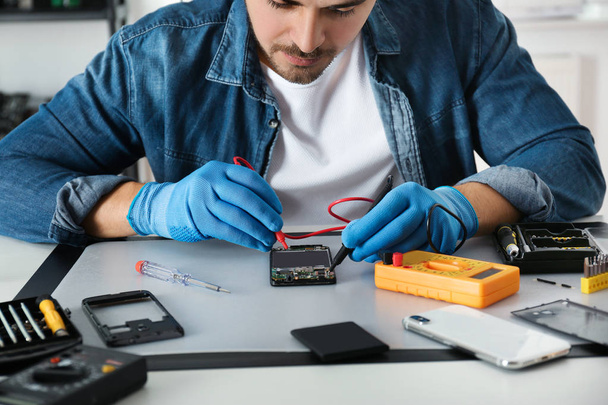 Technician checking broken smartphone at table in repair shop, closeup - Foto, immagini