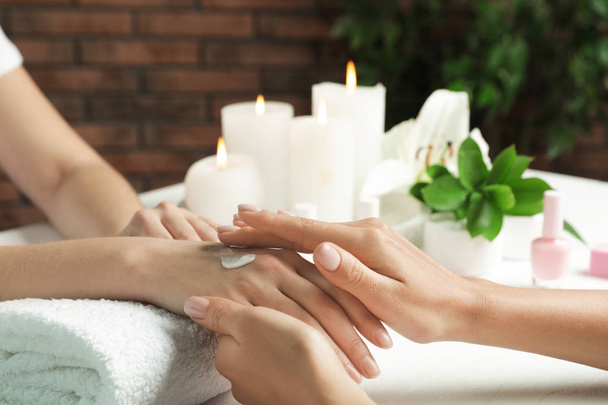 Cosmetologist aplicando creme na mão da mulher à mesa no salão de spa, close-up com espaço para texto
 - Foto, Imagem