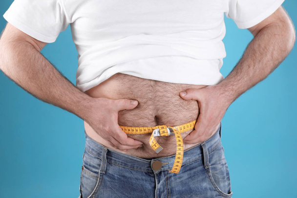 Overweight man with large belly and measuring tape on color background, closeup - Photo, image