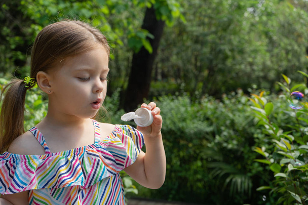 Cute little girl is blowing a soap bubbles in the garden - Fotoğraf, Görsel