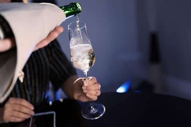 Waiter pouring champagne from bottle into woman's glass at bar, closeup. Space for text - Foto, imagen