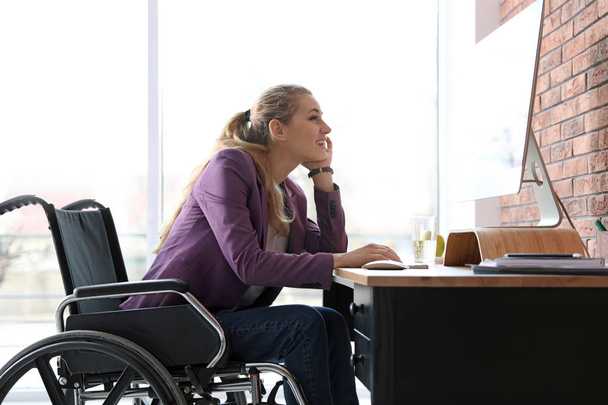 Woman in wheelchair working with computer at table indoors - Zdjęcie, obraz