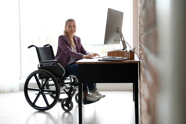 Woman in wheelchair working with computer at table indoors - Foto, Imagen