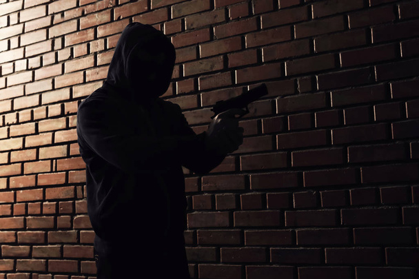 Man in hoodie with gun indoors. Dangerous criminal - Foto, Bild
