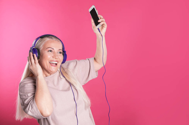 Mature woman in headphones with mobile device on color background. Space for text - Foto, Imagem
