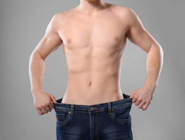 Young man with slim body in old big size jeans on grey background, closeup - Fotografie, Obrázek