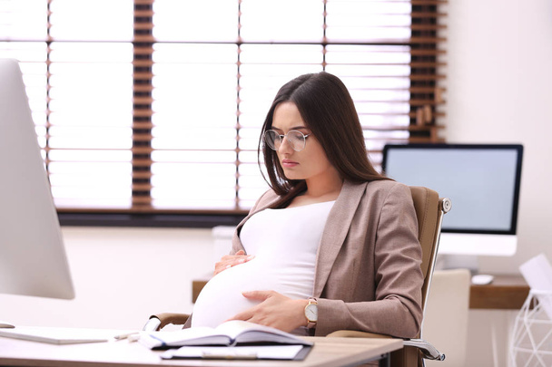Young pregnant woman suffering from pain while working in office - Foto, immagini