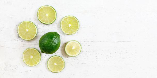 Foto de mesa, limão verde inteiro com frutas fatiadas ao redor, em placa de trabalho branca, espaço para o texto certo
 - Foto, Imagem