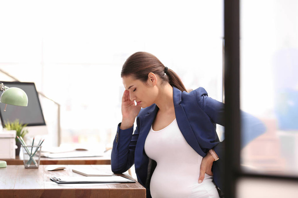 Young pregnant woman suffering from pain while working in office - Photo, image