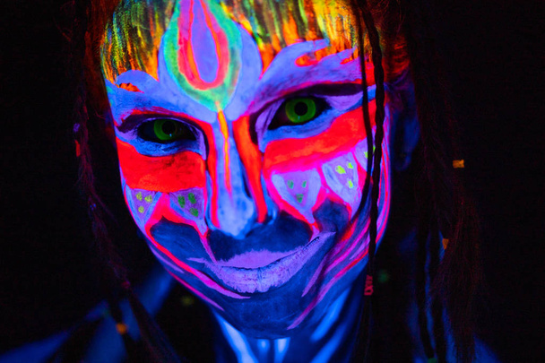 Blízký portrét mladé nahé ženy v modré zářící ultrafialové barvy a žluté oční čočky. Avatarova dívka Amazonka s copánky - Fotografie, Obrázek