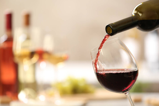 Pouring red wine from bottle into glass on blurred background. Space for text - Foto, imagen