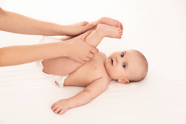 Mother and her cute child on white bed. Baby massage and exercises - Fotó, kép