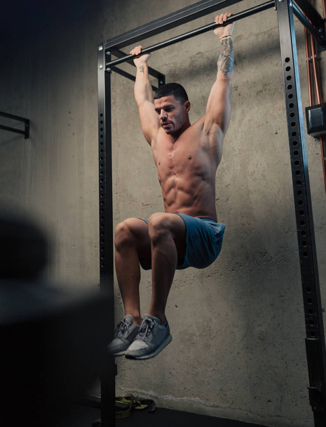 Young strong man in gym doing hanging abs exercise - Photo, image