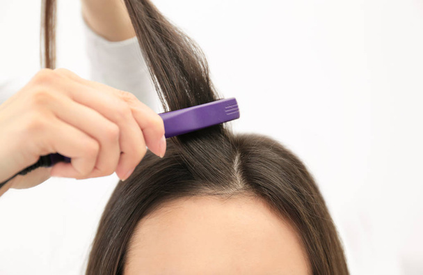 Hairdresser using modern flat iron to style client's hair in salon, closeup - Foto, Imagen