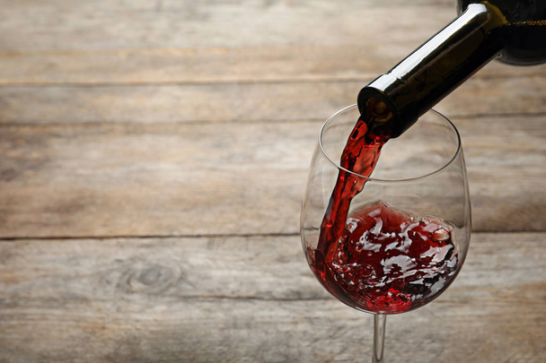 Nalewanie czerwonego wina z butelki do szklanki na drewnianym tle. Miejsce na tekst - Zdjęcie, obraz