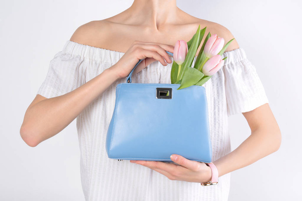 Stylish woman with handbag and spring flowers against light background, closeup - Foto, afbeelding