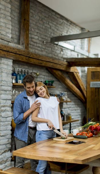 Lovely cheerful young couple cooking dinner together and having fun at rustic kitchen - Foto, imagen