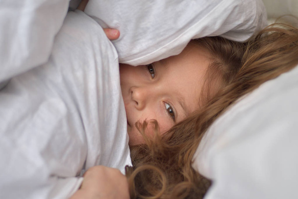 Маленькая девочка выглядывает из-под одеял. Hide-and-seek. Happy childhood concept.portrait
. - Фото, изображение