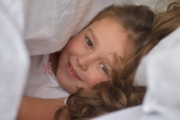 Маленькая девочка выглядывает из-под одеял. Hide-and-seek. Happy childhood concept.portrait
. - Фото, изображение