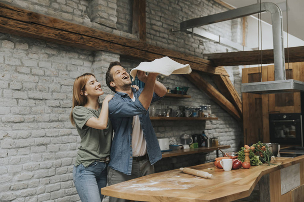 Young couple caking pizza in rustic kitchen together - 写真・画像