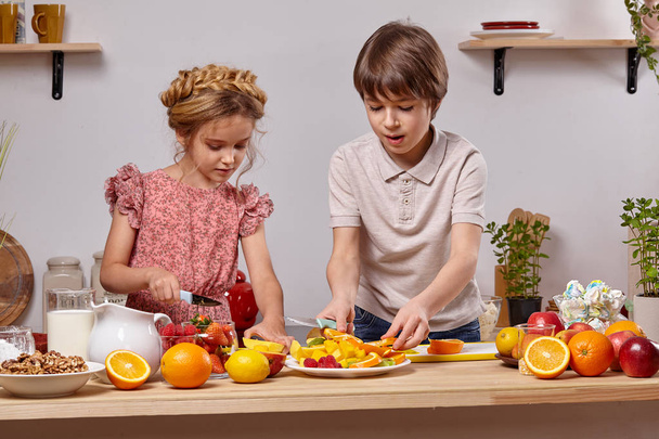 Lindos niños están cocinando juntos en una cocina contra una pared blanca con estantes en ella
. - Foto, imagen