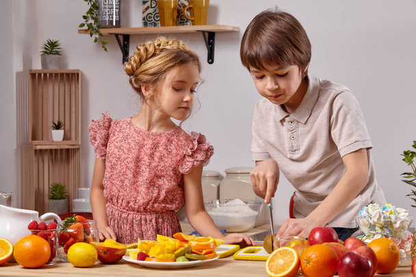Lindos niños están cocinando juntos en una cocina contra una pared blanca con estantes en ella
. - Foto, imagen