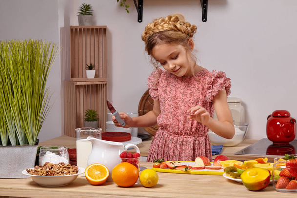 Nettes schönes Mädchen mit einer modernen Frisur kocht in einer Küche vor einer weißen Wand mit Regalen darauf. - Foto, Bild