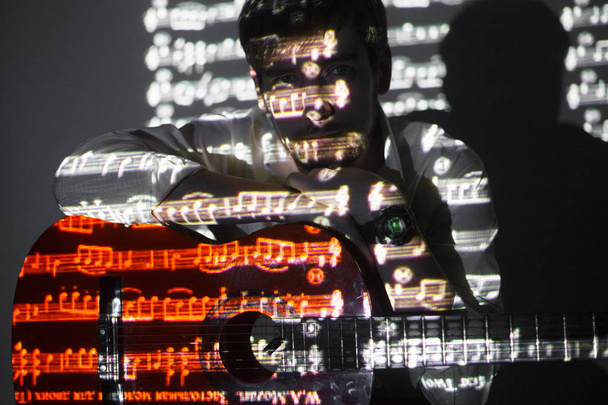 Πορτραίτο του μουσάτη κιθαρίστα με προβολή των σημειώσεων. Ο Μάνης κρατά την κιθάρα του και κοιτάζει την κάμερα - Φωτογραφία, εικόνα