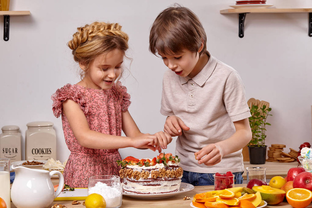 Little friends are making a cake together at a kitchen against a white wall with shelves on it. - Foto, Imagem