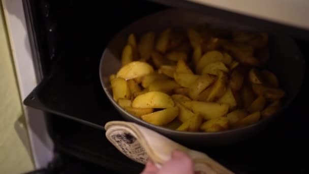 Female hand in a white pullover with a manicure using a white cloth slides a griddle of fried potatoes with spices on a baking sheet into the oven, closing the oven door and turns selector switch. - Materiaali, video