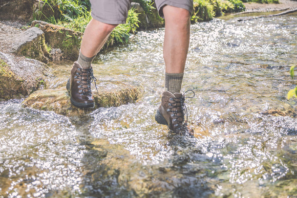 cropped shot of male hiker stepping on stones at rapid river - Fotoğraf, Görsel