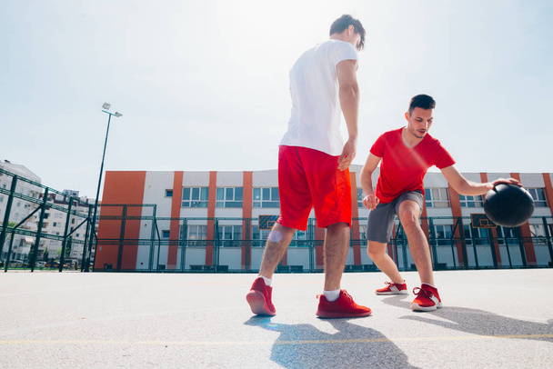 Two Caucasian friends wearing red sports equpment playing basket - 写真・画像