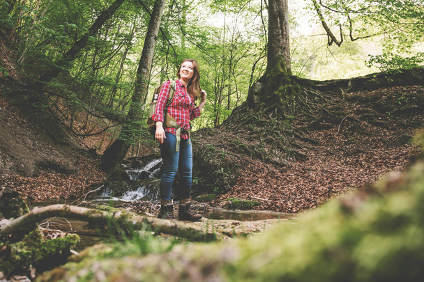 young woman with backpack hiking in beautiful forest near waterfall, low angle view - Photo, Image