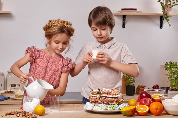 Маленькие друзья готовят торт вместе на кухне у белой стены с полками на ней
. - Фото, изображение