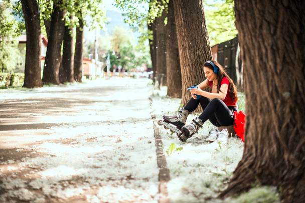 Девушка в синих наушниках готовится к катанию на роликах в парке
 - Фото, изображение